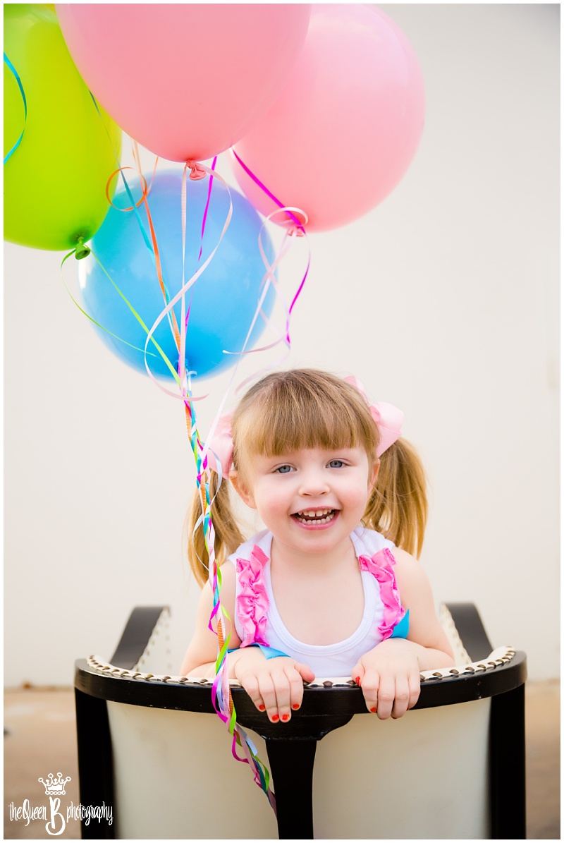 happy pig-tailed girl peering over back of chair with balloons
