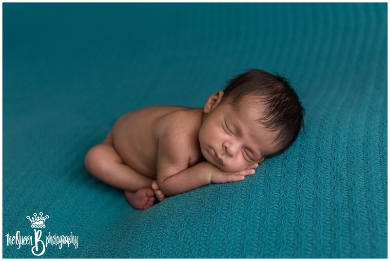 curled up sleeping newborn boy on teal blue background