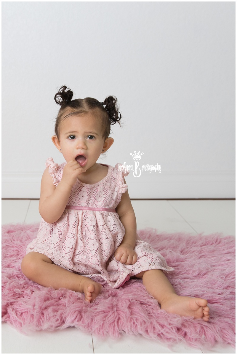 adorable baby girl with pigtails on pink furry rug in white studio photo shoot