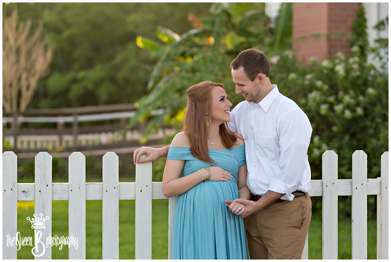 Happy couple poses for romantic Maternity Portraits bu white picket fence