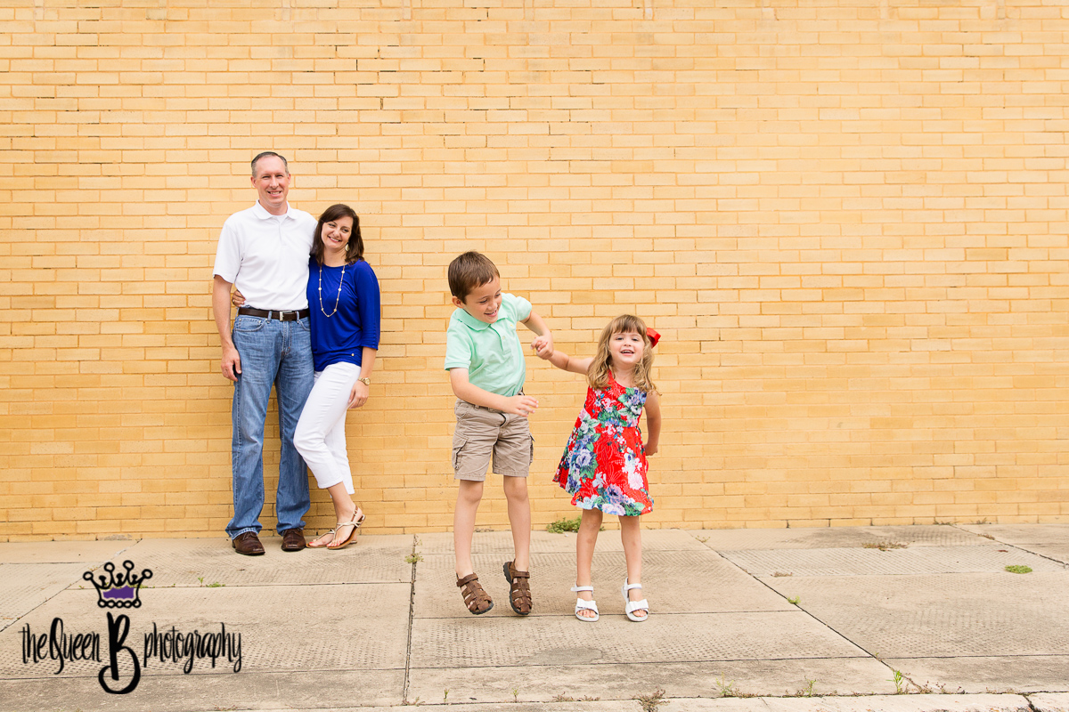 siblings playing in front of mom and dad against yellow brick wall in Richmond Texas
