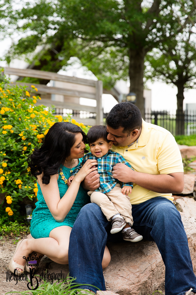adorable family snuggling baby boy at park with yellow flowers in background