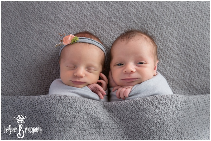 newborn fraternal twins snuggled under gray blanket