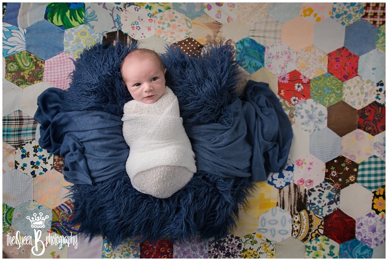 awake newborn baby boy on multicolored patchwork quilt